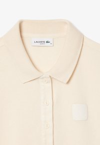 Crème-kleurig poloshirt met een textuurstof, een klassieke kraag, knoopsluiting en een klein wit logo-op-patch op de borst.