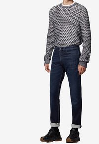 Maglione lavorato a maglia con motivo geometrico blu navy e bianco; abbinato a jeans di denim scuri; sneakers nere con suole in gomma; polsini arrotolati.