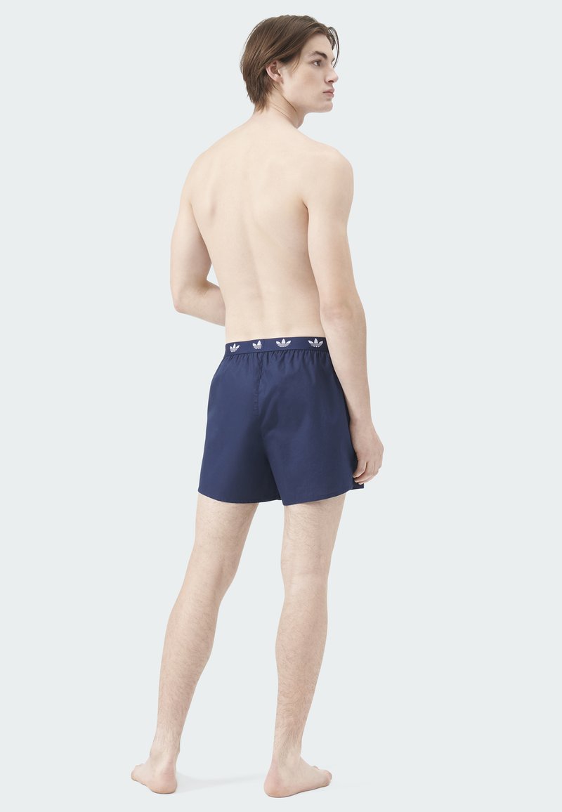 Marineblaue Badeshorts mit elastischem Bund, oben mit weißem Logomuster. Glatte Textur, knielanger Schnitt, lässiges Design.