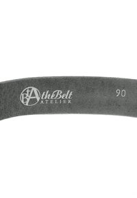 Grå mockarem bälte med präglad "At the Belt Atelier"-logotyp och storlek "90" på insidan. Slät textur och böjd form.