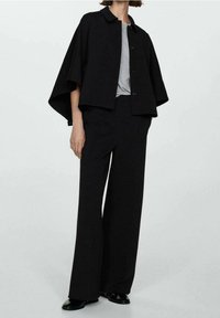 Veste noire courte avec un col et fermeture à boutons, associée à un pantalon large noir et un t-shirt basique gris. Tissu lisse.