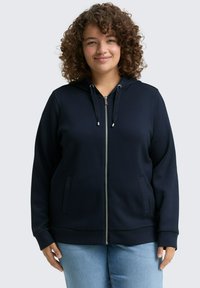 Sudadera con cremallera en color azul marino, con acabado texturizado, capucha con cordón y bolsillos laterales. Presenta una cremallera metálica y puños acanalados.