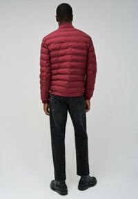 Chaqueta de plumas burdeos con costuras horizontales, puños acanalados y cuello. Combinada con jeans negros y botas negras. Diseño sencillo y aerodinámico.