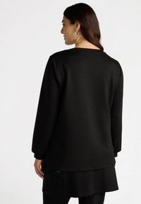 Sudadera negra de manga larga, con cuello redondo y un corte relajado. Suave tela con una textura sutil; combinada con una falda a juego.