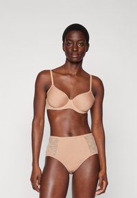 Nude bra with seamless cups and adjustable straps, paired with high-waisted panties featuring lace side panels. Smooth fabric texture.