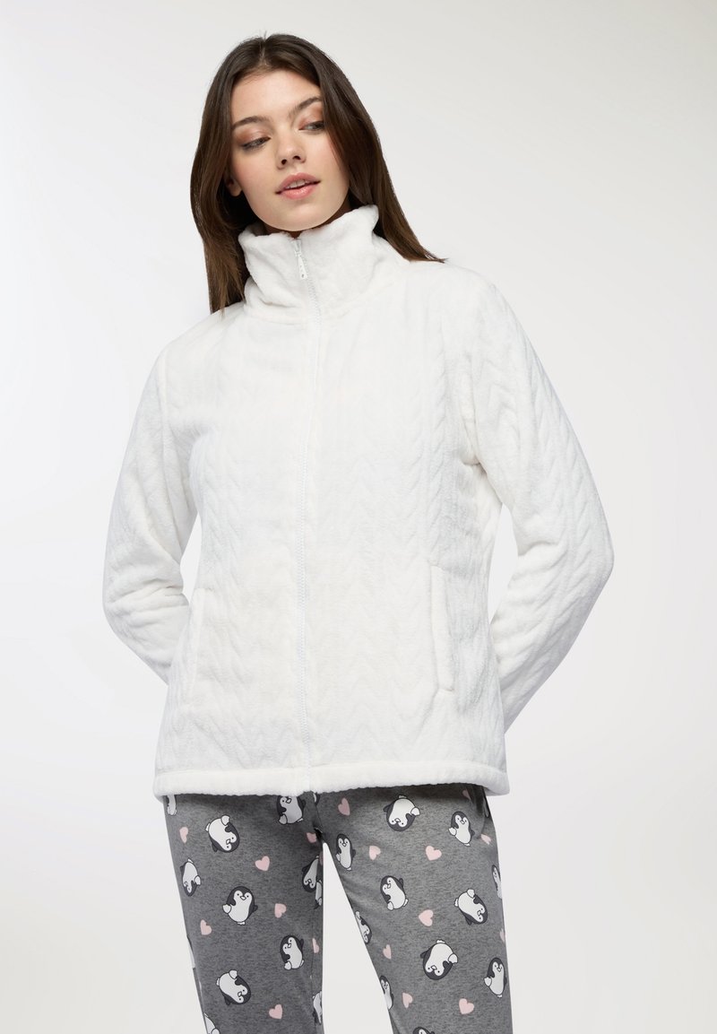 Biała polarowa kurtka z wysokim kołnierzem, z wzorem w warkocze i bocznymi kieszeniami, w połączeniu z szarymi legginsami w nadruk z pingwinami.