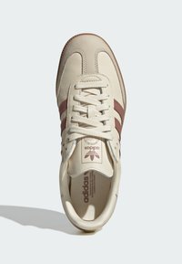 Beige joggesko med brune striper, skinn-overdel og gummisåle. Har detaljer med sømmer og en merket tungeetikett.