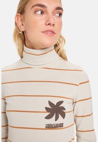 Pull à col roulé à manches longues en beige clair, avec des rayures orange horizontales et un logo en forme de feuille brune avec le texte "Quiksilver" sur la poitrine.