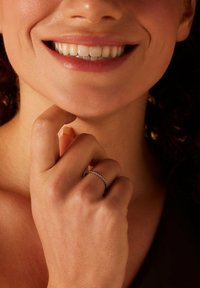 Zilverkleurige ring met een kralenontwerp, gedragen aan een vinger, hand die de kin aanraakt. Close-up van een glimlach en natuurlijke huidtextuur.