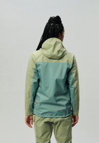 Giacca con cappuccio in verde bicolore: parte superiore in oliva chiaro e parte inferiore in teal. Tessuto morbido e leggero con un design aderente e polsini elasticizzati.