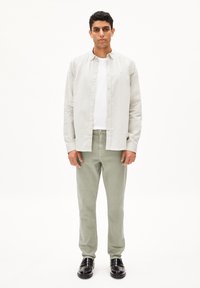 Chemise gris clair à boutons sur un t-shirt blanc, assortie à un pantalon vert clair et des chaussures noires. La chemise a un col classique et des manches longues.