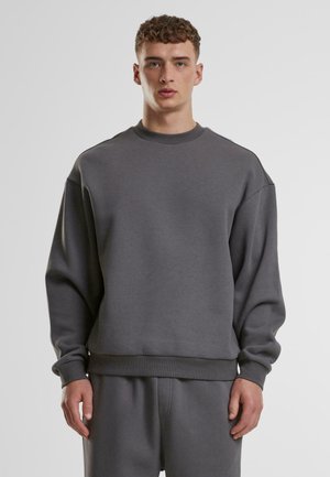 Sudadera gris con cuello redondo, hombros caídos y puños de canalé. Fabricada con un tejido suave, presenta un corte relajado y un diseño minimalista.