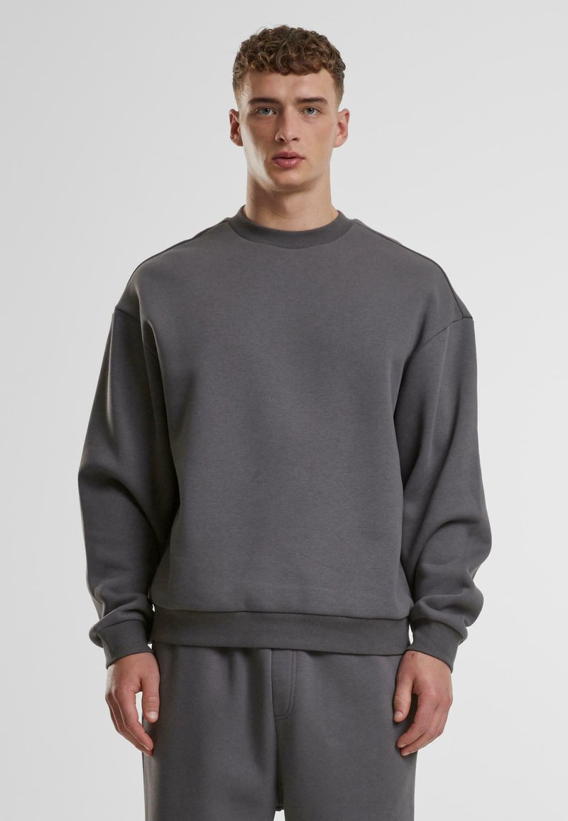 Felpa grigia con scollo rotondo, spalle dropped e polsini in costina. Realizzata in tessuto morbido, presenta una vestibilità comoda e un design minimal.