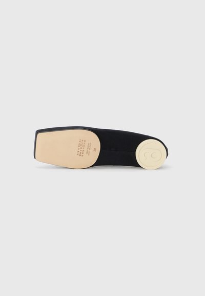 Black suede flat shoe with a smooth beige sole. The sole features a circular logo and embossed size details near the heel.
