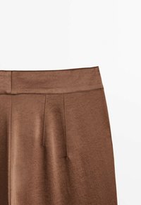 Jupe marron taille haute avec des détails subtils de coutures verticales, texture lisse et une large ceinture sur fond blanc.