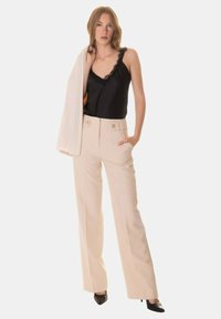 Pantaloni beige a vita alta con gambe ampie, dotati di tasche laterali e doppi bottoni. Abbinati a un top in raso nero con pizzo.