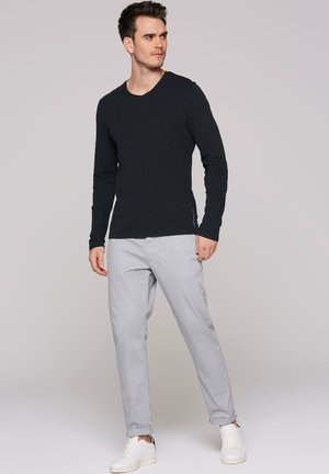 Schwarzes Langarmshirt, Slim Fit, graue Hose, hochgekrempelte Bündchen, weiße Sneaker, lässiges Design, glatter Stoff, dezentes Markenlogo.