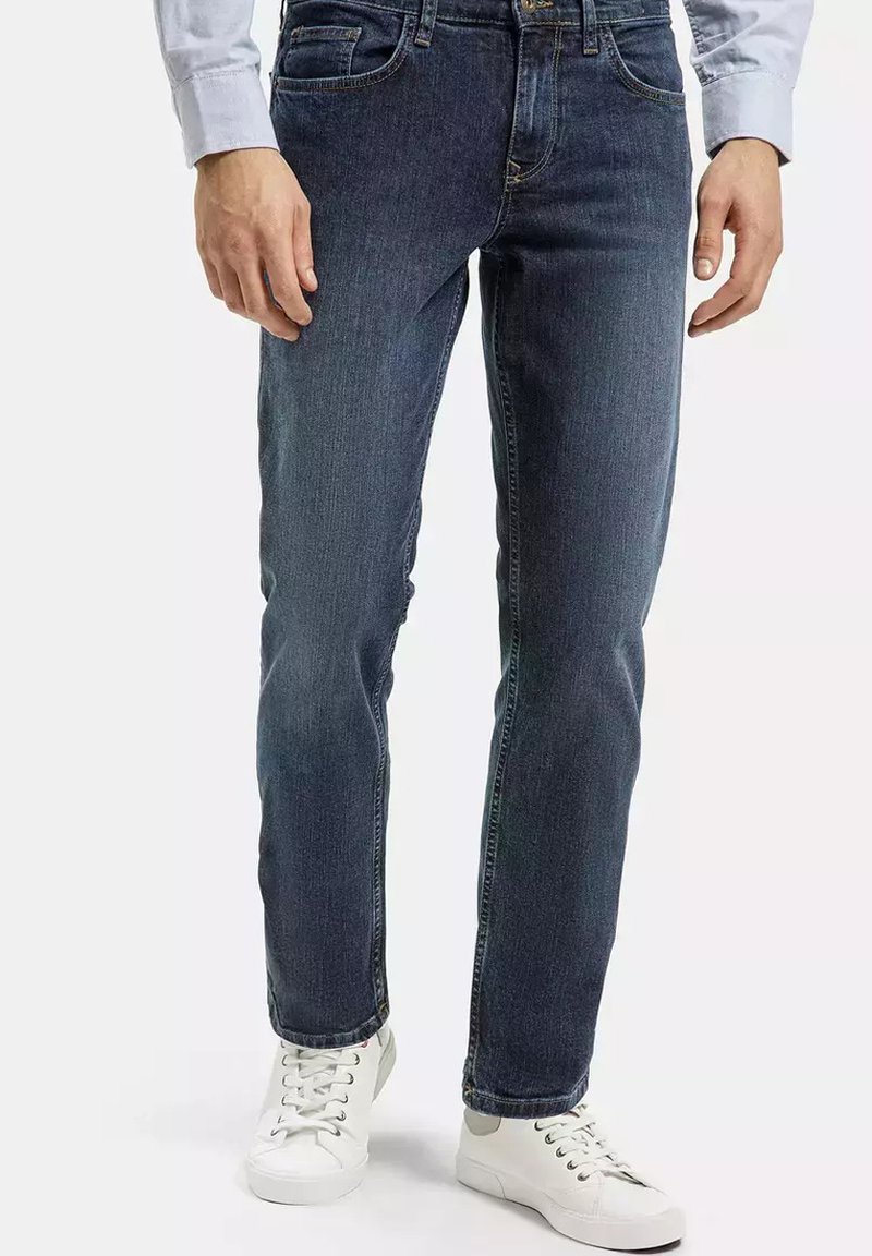 Granatowe dżinsy ze prostymi nogawkami, z pięcioma kieszeniami i subtelnym przeszyciem. Połączone z białymi trampkami.