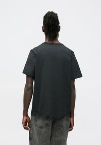 Μαύρο βαμβακερό μπλουζάκι με στρογγυλή λαιμόκοψη και κοντά μανίκια, με χαλαρή εφαρμογή. Το ύφασμα φαίνεται ομαλό χωρίς εμφανή σχέδια.