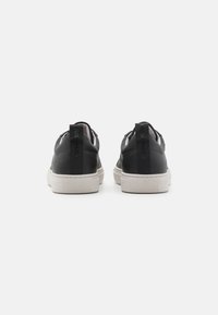 Sneakers in pelle nera con suola in gomma bianca, dotati di un contrasting pull-tab nero e dettagli di cucitura sul retro.