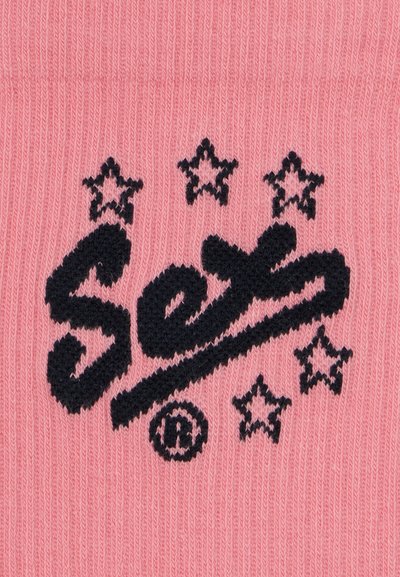 Tecido de malha rosa com texto bordado em preto "Sexo" e estrelas decorativas, exibindo uma textura suave e um contraste de cores vibrante.