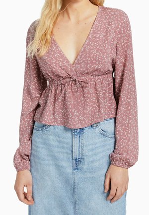 Blush-farbene Bluse mit kleinen weißen Blumenmustern, tiefem V-Ausschnitt, geraffter Taille und langen Ärmeln mit elastischen Bündchen, kombiniert mit einem hellblauen Jeansrock.