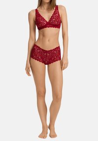 Krajková braletka a nízké kalhotky v tmavě červené barvě. Zvlněné okraje a průhledná květinová krajka zvýrazňují strukturovaný vzhled.