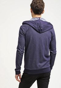 Felpa blu navy realizzata in tessuto morbido, con un colletto interno grigio chiaro a contrasto. Presenta una vestibilità standard e polsini e fondo a costine.