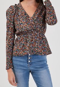 Blommig blus med djup V-ringning, långa ärmar och rynkad midja. Har flerfärgade blommor på en mörk bakgrund. Parat med blå jeans.