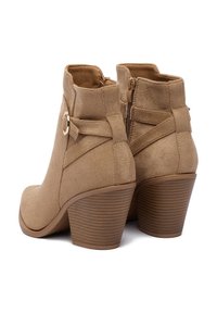 Beżowe zamszowe botki za kostkę na słupku, z bocznym zamkiem oraz ozdobnym paskiem z detalem w złotym odcieniu.