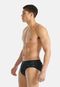 Czarne kąpielówki z geometrycznym wzorem w różnych odcieniach ciemnej szarości, z gładkim elastycznym pasem i dopasowanym krojem.