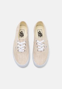 Baskets en toile beige à finition texturée, lacets blancs et semelle en caoutchouc. Marque visible sur la semelle intérieure et l'étiquette latérale.