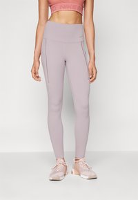 Leggings taille haute violettes claires avec deux poches latérales, design ajusté et texture lisse, associés à des chaussures de sport roses claires.