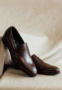 Bruine leren loafers met een gladde afwerking, penny strap details en gestikte accenten op de neus. Lage hak en ronde vorm.