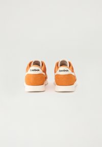 Oransje semskede sneakers med en hvit mellomsåle og beige detaljer. Har en logo på hælen og et rundt tådesign.