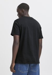 Tricou negru din bumbac cu mâneci scurte, guler rotund, textură netedă și croială lejeră, asortat cu șorturi din denim bleu.