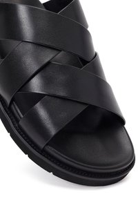 Czarna skórzana sandał z szerokimi, krzyżującymi się paskami oraz wyściełanym podbiciem na grubej gumowej podeszwie.