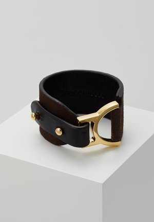 Dunkelbraunes Lederarmband mit schwarzem Riemen und goldener Metallschnalle, auf einer weißen Oberfläche vor hellgrauem Hintergrund platziert.