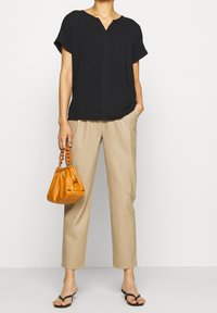 Sort kortærmet bluse med v-hals, beige skræddersyede bukser og en orange læderhåndtaske med kædehåndtag. Sorte flip-flops fuldender looket.