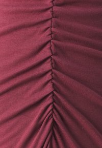 Burgundy szövet, amelyen függőleges redők találhatók a középen, sima, puha tapintással és finom bordázott mintával.