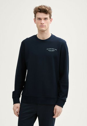 Sudadera de manga larga color azul marino con textura acanalada, cuello redondo y estampado de logo en el lado izquierdo del pecho. Presenta un dobladillo recto y mangas con puños.