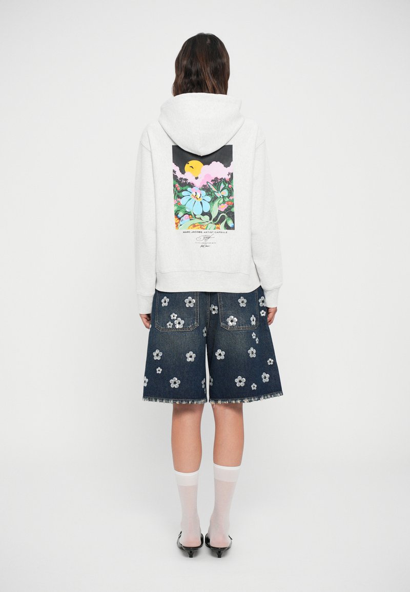 Siv hooded sweatshirt z rožnatim grafičnim motivom na hrbtu, v kombinaciji z jeans krilom, ki ima bele in srebrne cvetne aplicirane ter razfrkane robove. Bele nogavice in petke.