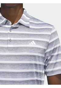 Šedá a biela pruhovaná polo košeľa s golierom, zapínaním na tri gombíky a malým bielym logom Adidas na hrudi, s textúrovanou tkaninou.