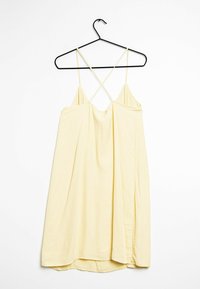Ein gelbes Slipkleid an einem schwarzen Kleiderbügel, mit dünnen Überkreuz-Trägern, lockerer Passform und einer weichen Textur mit abgerundetem Saum.