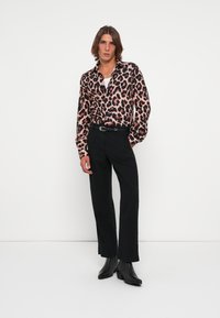 Leopard print long-sleeve shirt in shades of pink and black, paired with black trousers and black ankle boots, featuring a classic collar and belt.