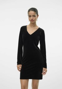 Robe en velours noir avec des manches longues, un décolleté en V, une silhouette ajustée et un éclat subtil. Design minimaliste, texture lisse, longueur au genou.