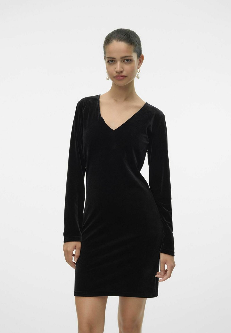 Robe en velours noir avec des manches longues, un décolleté en V, une silhouette ajustée et un éclat subtil. Design minimaliste, texture lisse, longueur au genou.