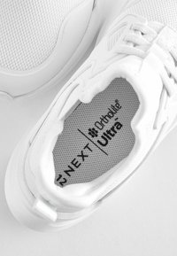 Weiße Sportschuh mit einem Obermaterial aus Mesh, gepolstertem Innenraum mit Ortholite® Ultra-Logo und einer strukturierten Sohle für besseren Halt.