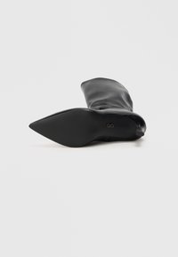 Crna kožna gležnjača s oštrim vrhom, mekim teksturom i uskim, protukliznim đonom. Ima elegantan, minimalistički dizajn.
