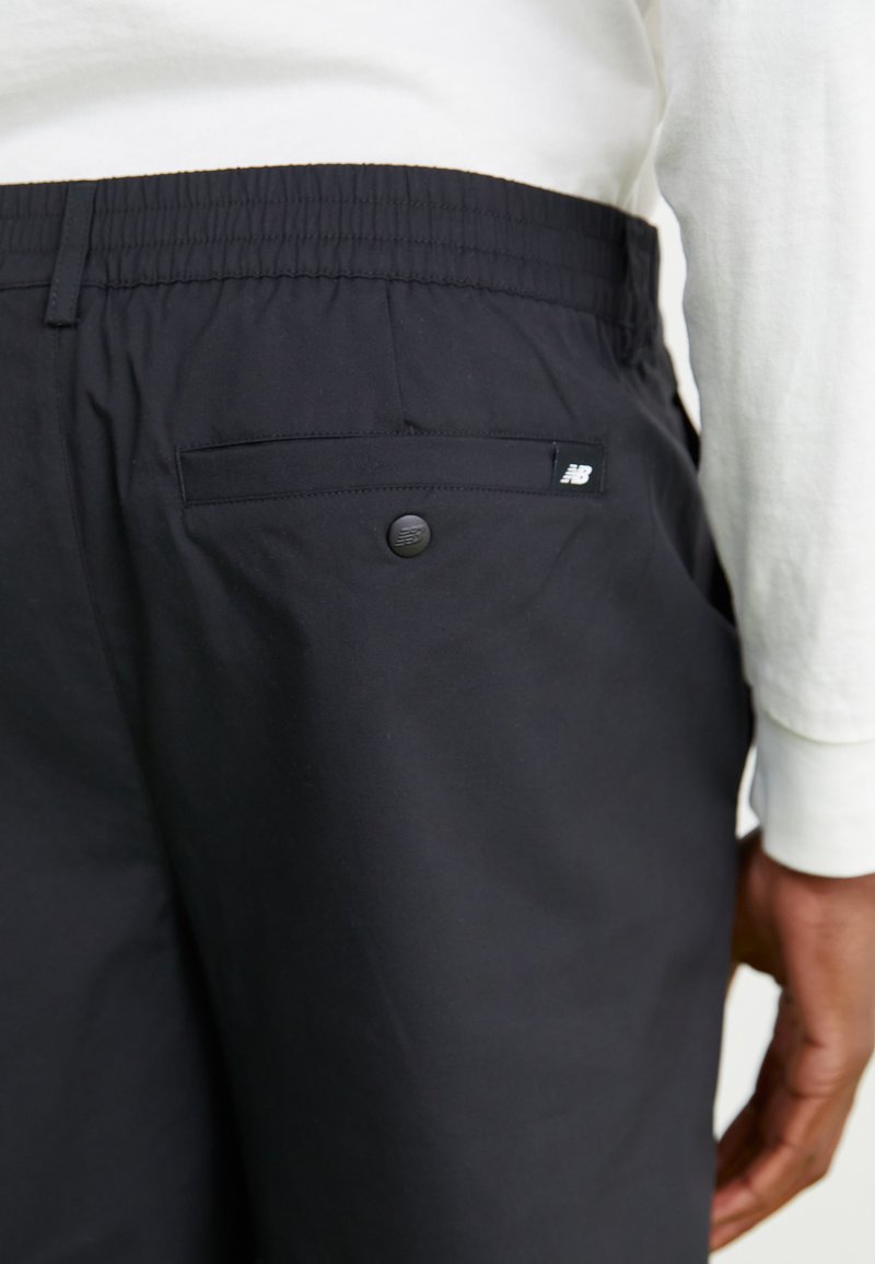 Schwarze Hose aus leichtem Stoff mit elastischem Bund. Hat eine Gesäßtasche mit einem schwarzen Knopf und einem kleinen Logotag an der Tasche.